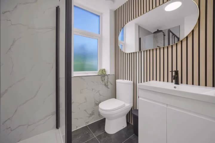 Shower room with marble-effect walls, oak slat panelling and round illuminated mirror