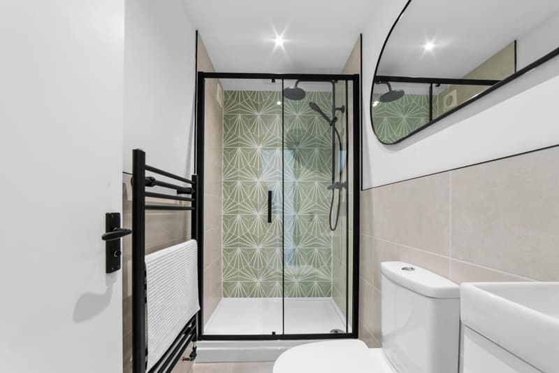 HMO shower room with black-framed glass enclosure, patterned tiles and round mirror