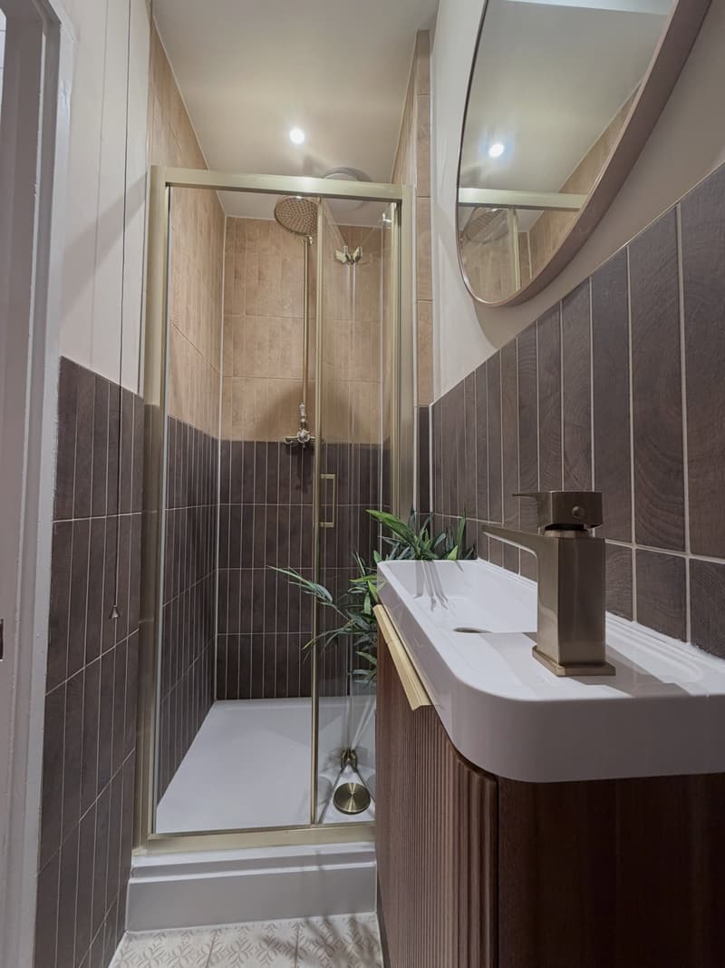 Second bathroom with two complementary brown tiles, round mirror and traditional brass fittings