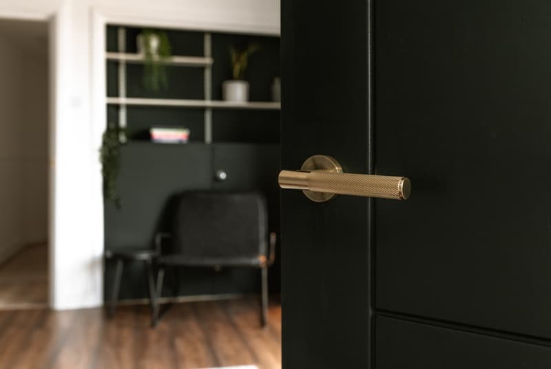 Dark green panelled door with brass lever handle and a study nook beyond