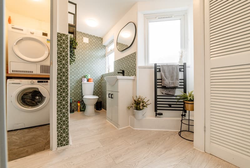 Stacked laundry cupboard with louvred doors beside a green-tiled bathroom